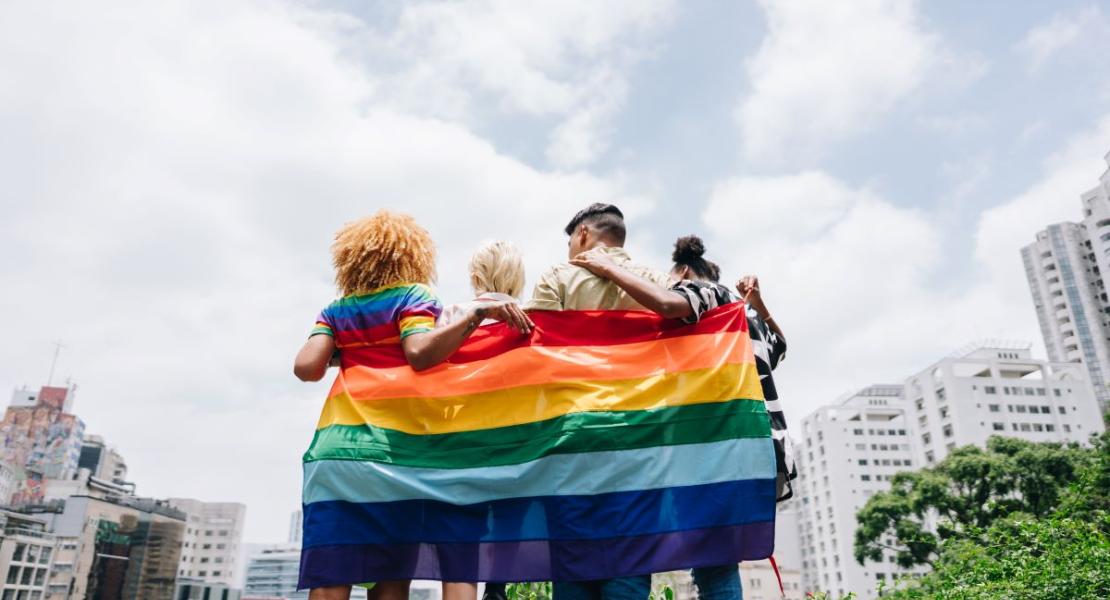 Group of people wrapped in a rainbow flag.
