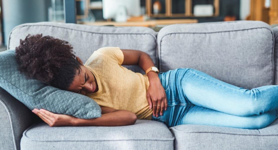 a young woman experiencing stomach pain while lying on the sofa at home