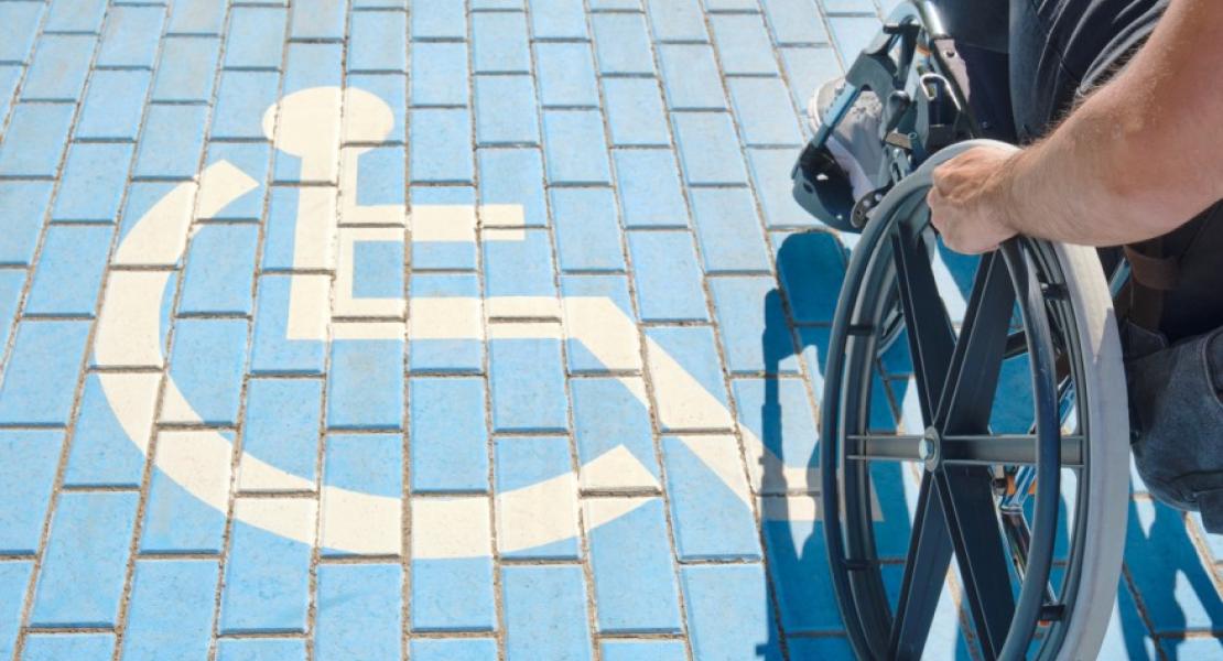 A person using a wheelchair on blue brick pavement next to a painted accessibility symbol.