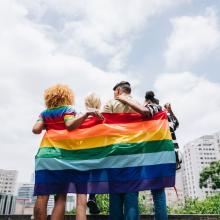 Group of people wrapped in a rainbow flag.