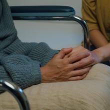 two people sitting down holding hands supporting each other 