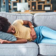 a young woman experiencing stomach pain while lying on the sofa at home