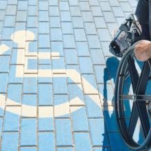 A person using a wheelchair on blue brick pavement next to a painted accessibility symbol.